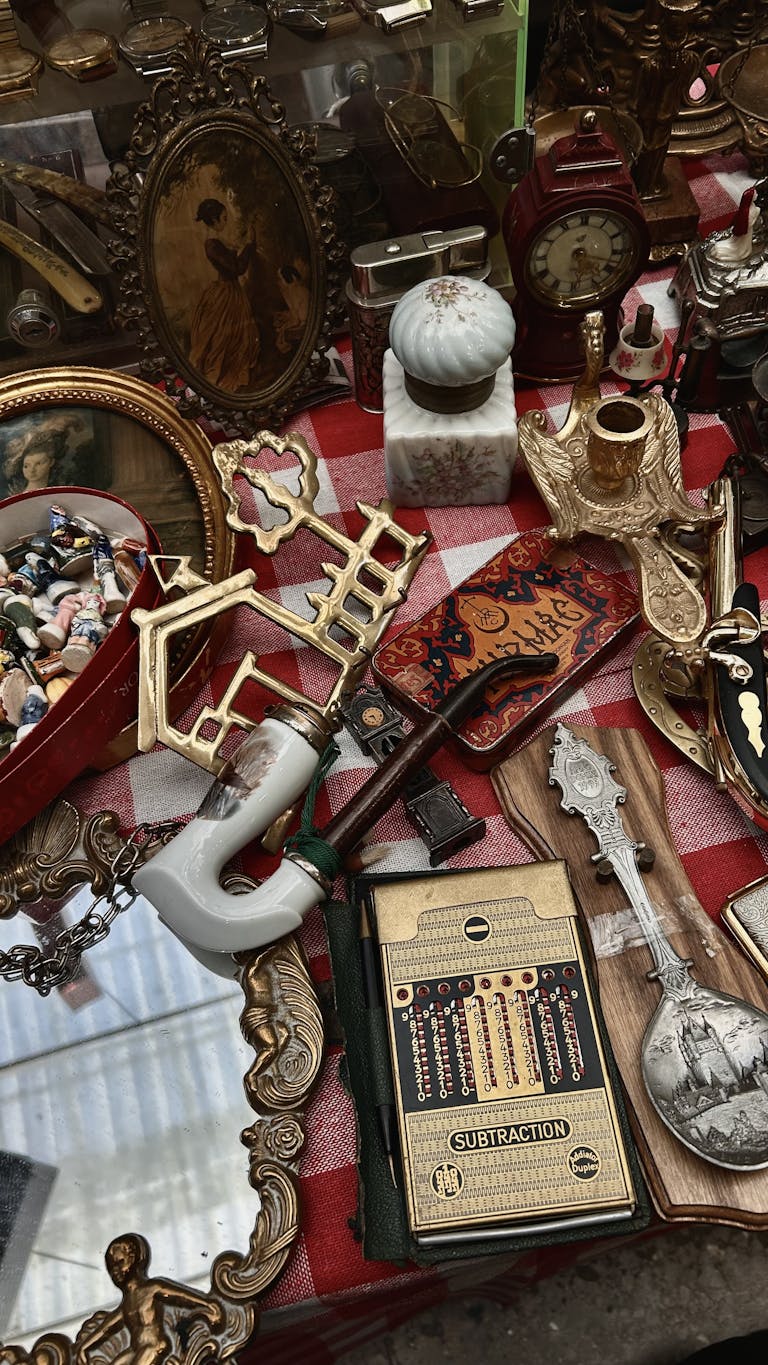 Assorted antique items displayed on a red checkered tablecloth at a market.